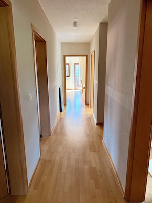 Ein Flur mit Holzboden, Türen an beiden Seiten und Blick in einen angrenzenden Raum mit einem Fenster.
