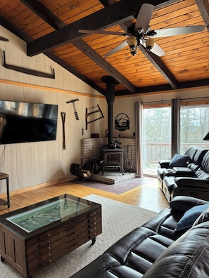 A cozy living room with a fireplace, leather sofa, wooden ceiling beams, and a glass coffee table.