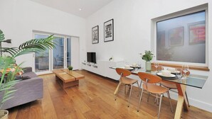 Uma sala de estar moderna com um sofá, uma mesa de jantar com cadeiras, uma televisão e quadros nas paredes.