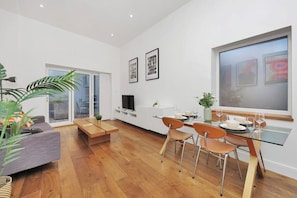 A modern living room with a sofa, a dining table with chairs, a TV, and framed pictures on the wall. - 1-bed flat in Broadway Market, Hackney (London)