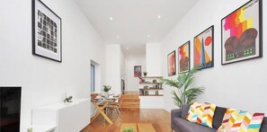 Uma sala de estar moderna com um sofá, um espaço de refeições com mesa e cadeiras, e uma escada que leva a um andar superior.