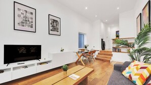 Uma sala de estar moderna com televisão de tela plana, mesa de centro de madeira, sofá cinza e almofadas coloridas.