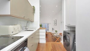 Cozinha compacta com micro-ondas, pia e máquina de lavar, que dá acesso a uma área de refeições com mesa e cadeiras.