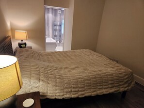 Ein Schlafzimmer mit einem Bett, einem Nachttisch mit Lampe, einem Fenster mit Blick und einer Tür.