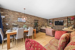 A dining area with a brick wall, a wooden table, and chairs. - 5 Bed/2 Bath Private House with Balcony - London (London)