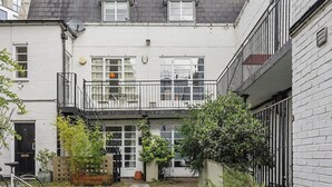 A white two-story building with a balcony, a door, and a small garden area with plants. - 5 Bed/2 Bath Private House with Balcony - London (London)