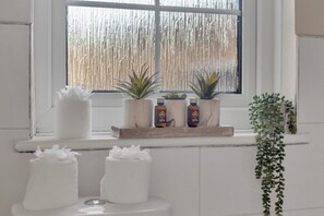 Ein Badezimmer mit Fenster, einer Pflanzenablage und zwei weißen Behältern.