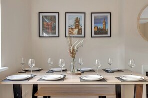 Ein Esstisch ist für sechs Personen gedeckt, im Hintergrund sind gerahmte Bilder von Londoner Sehenswürdigkeiten an der Wand zu sehen.