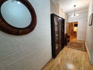 A hallway with a white brick wall, a wooden floor, a large mirror, a glass cabinet, and a patterned rug. - 3-bedroom spacious apartment in Shoreditch (London)