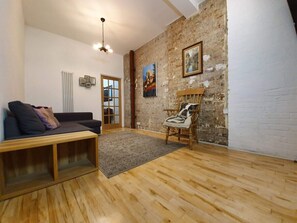 A room with a wooden floor, a sofa, a chair, a radiator, and a door. - 3-bedroom spacious apartment in Shoreditch (London)