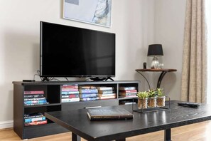 Ein modernes Wohnzimmer mit Flachbildfernseher, Couchtisch, Bücherregal und einem kleinen Beistelltisch mit Lampe.