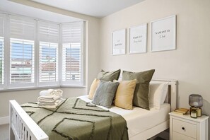 Ein Schlafzimmer mit einem Bett, Kissen, einem Nachttisch mit Lampe und einem Fenster mit Jalousien.