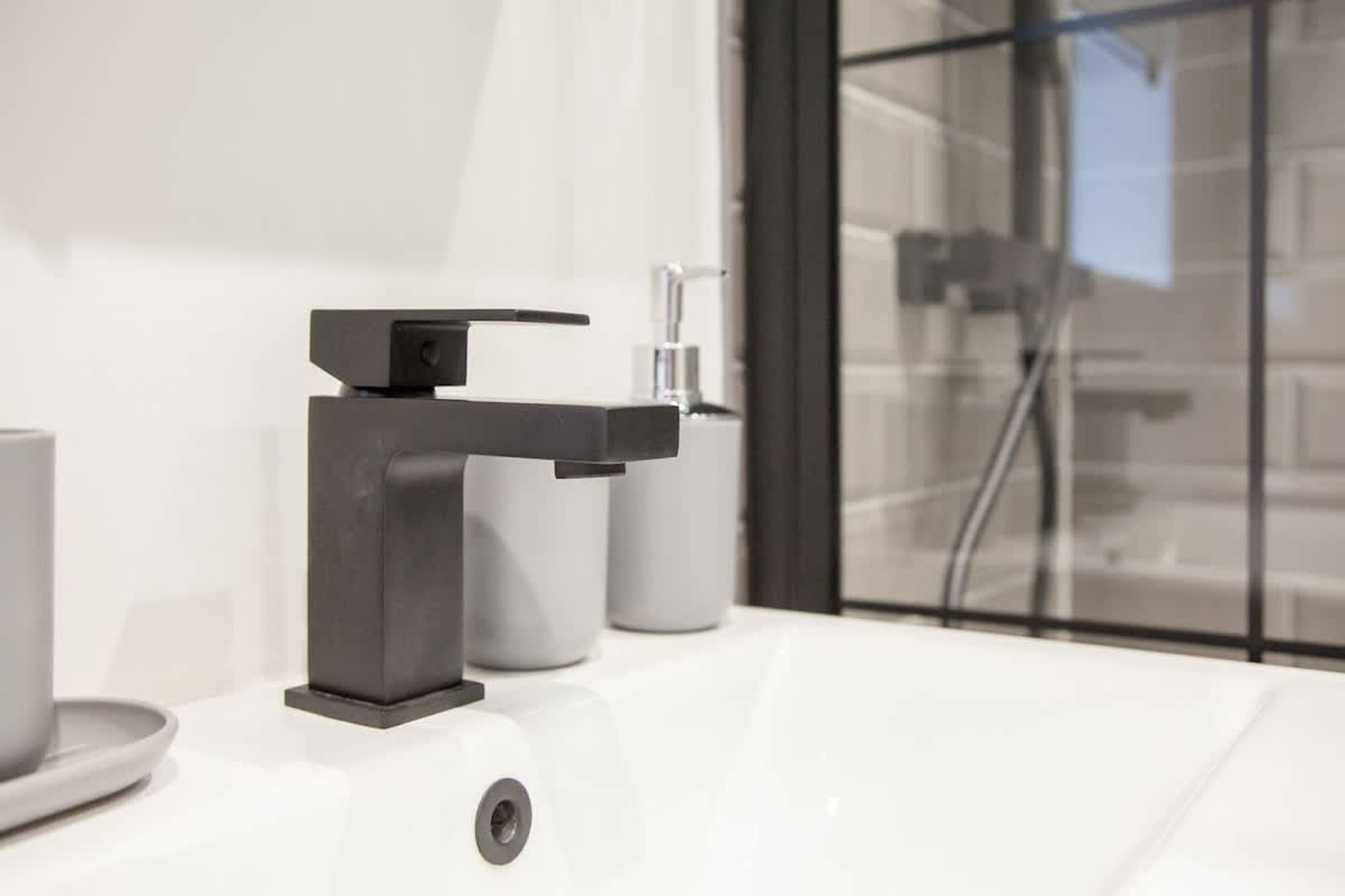 Ein modernes Badezimmer mit einem weißen Waschbecken, einem schwarzen Wasserhahn und einer Duschkabine aus Glas.