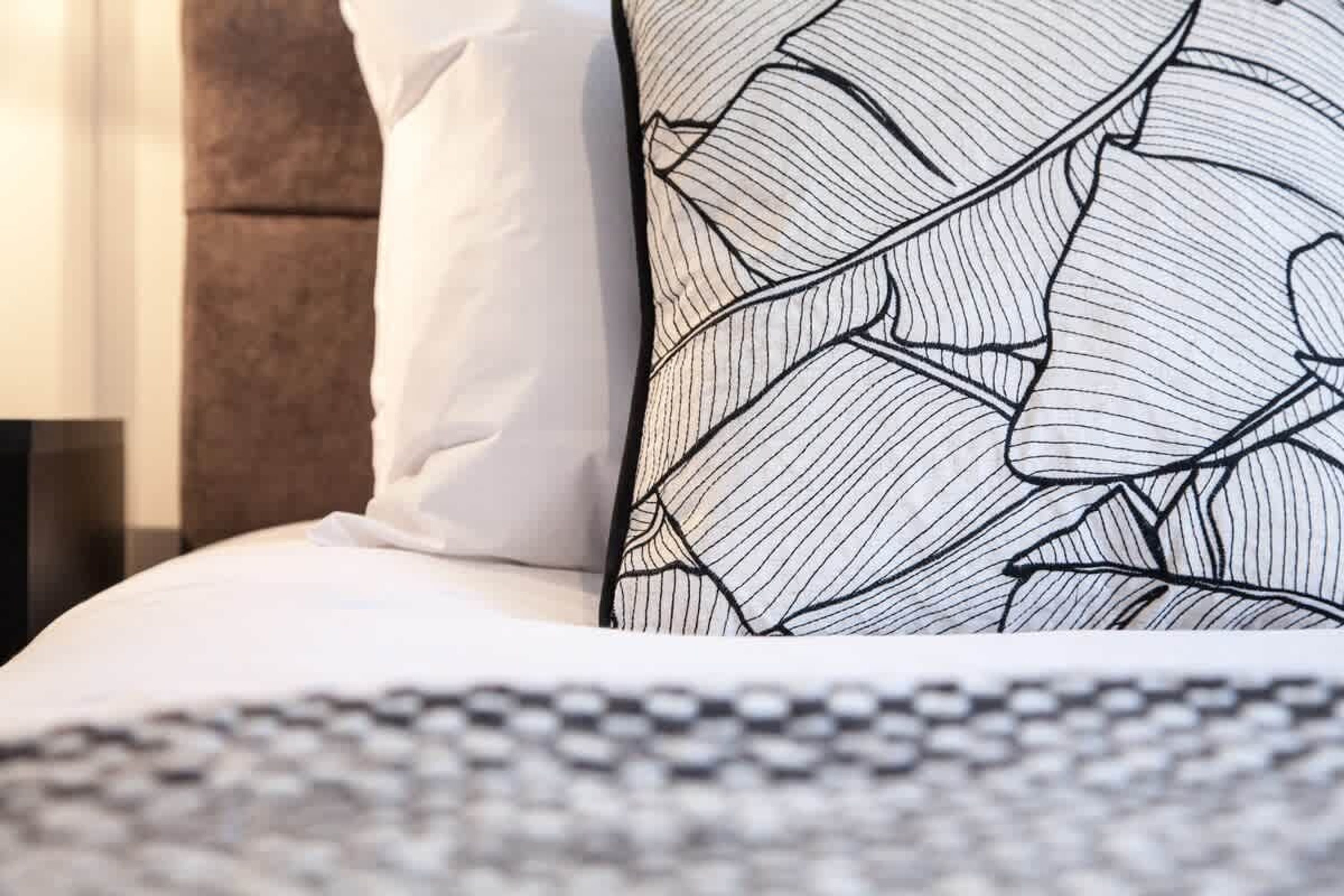 A bed with white bedding and a patterned pillow.