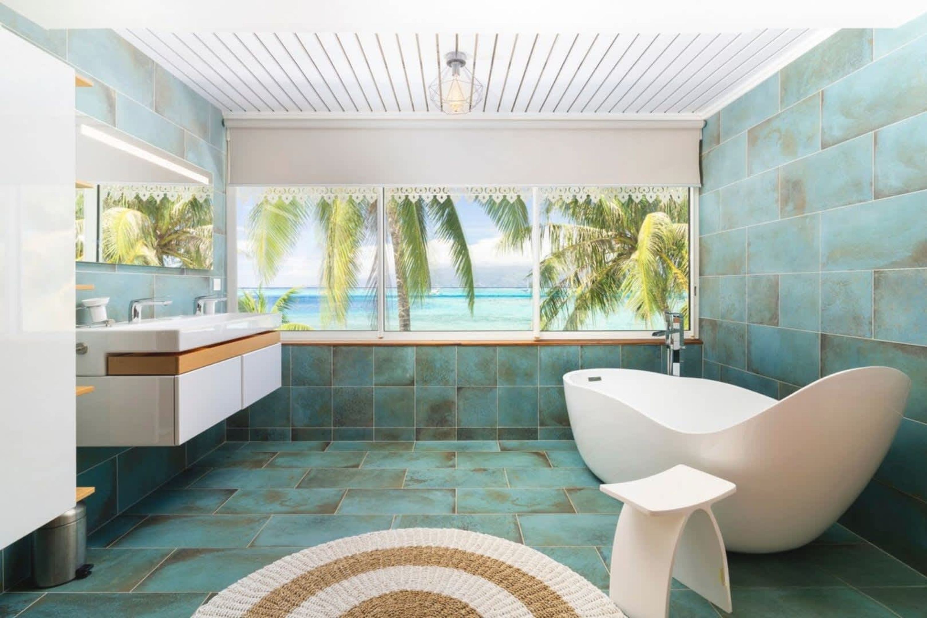 A modern bathroom with a view of the ocean, a freestanding bathtub, and a large mirror.