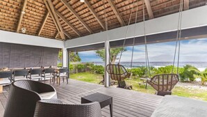 A covered outdoor area with a wooden deck, wicker furniture, and a view of the ocean. - Coastal Bliss 1BR Bungalow by the Sea in Moorea (Moorea-Maiao)
