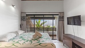 A bedroom with a bed, a TV, a wooden ceiling, and a view through a sliding door. - Coastal Bliss 1BR Bungalow by the Sea in Moorea (Moorea-Maiao)