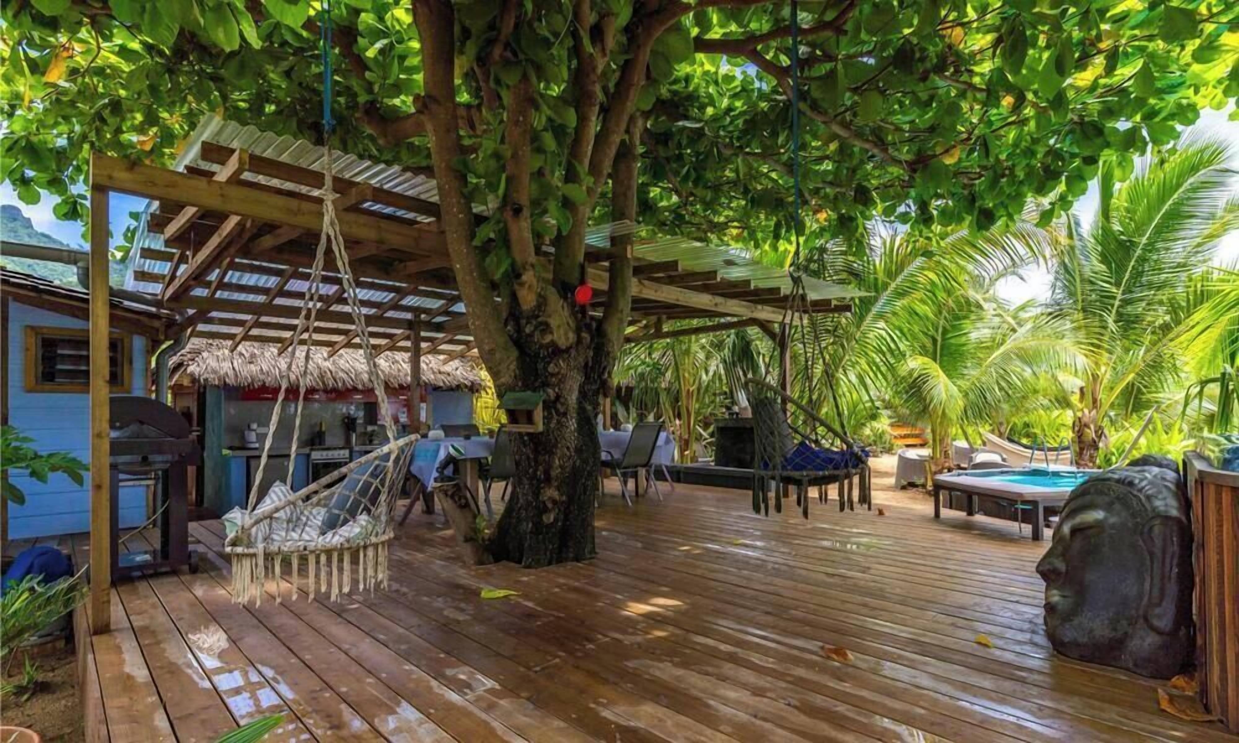 A wooden deck with a thatched-roof structure, outdoor seating, and a pool area.
