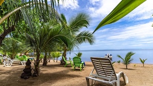 A beach with lounge chairs, palm trees, and a boat on the water.