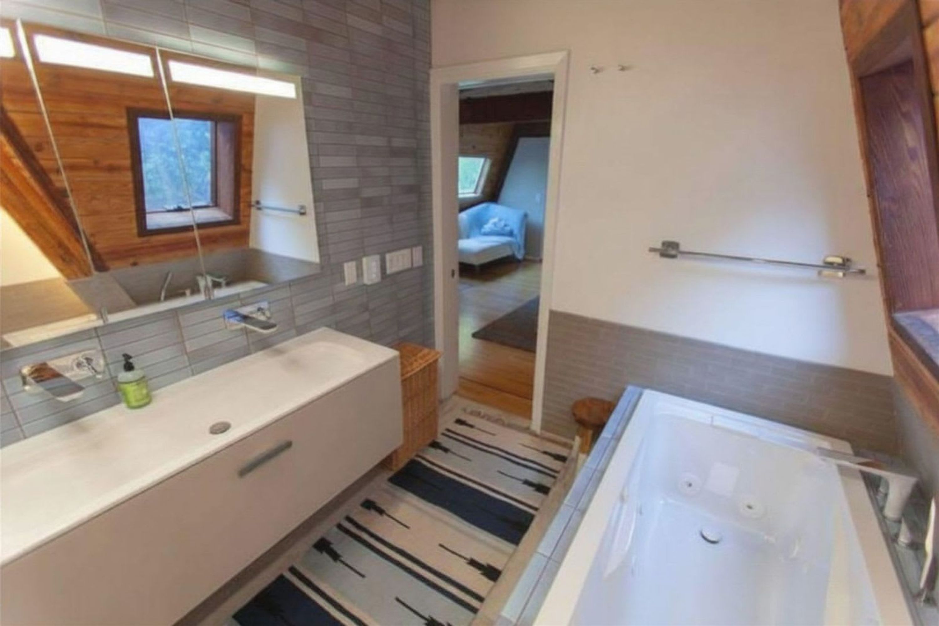 Une salle de bain moderne avec une grande baignoire, un miroir et une fenêtre.
