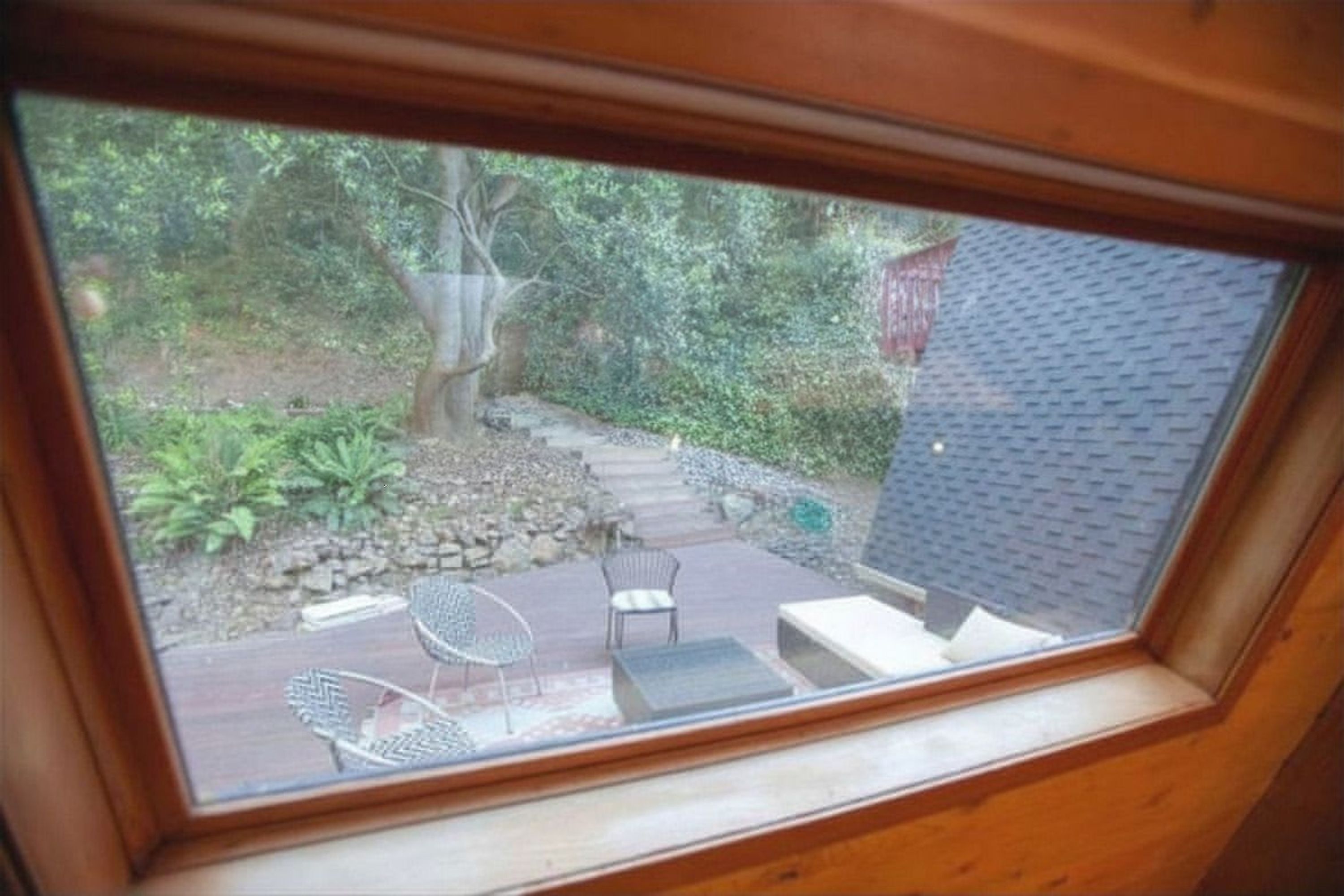 A view through a window of a patio area with outdoor furniture, a stone pathway, and a building with a dark roof.