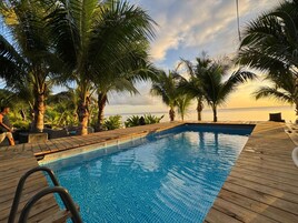 Una piscina con cubierta de madera, rodeada de palmeras y vistas al océano.