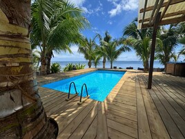 Una terraza de madera con piscina, rodeada de palmeras y vistas al océano.