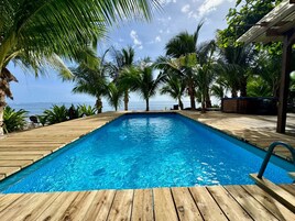 Una terraza de madera con piscina, rodeada de palmeras y vistas al océano.