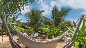A hammock in a tropical garden with a thatched roof structure and various plants. - Chic Beachside Retreat (Moorea-Maiao)