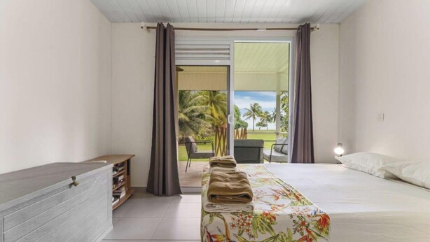 A hotel room with a bed, a bedside table, a chair, and a view of the outdoors. - Seaside Paradise Retreat - 3BR House in Moorea (Moorea-Maiao)