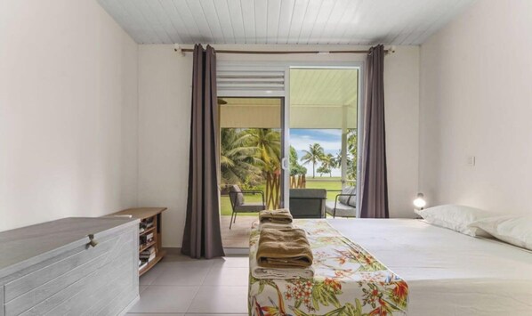 Quarto com cama, mesa de cabeceira, guarda-roupa e vista para um jardim através de uma porta deslizante.