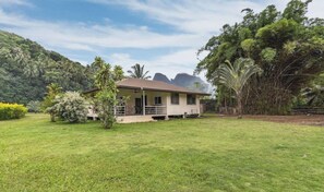 Uma casa térrea com telhado plano, cercada por um gramado bem cuidado e várias árvores.