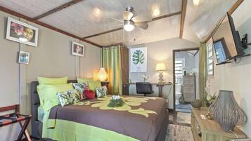 Een slaapkamer met een bed, een bureau, een stoel, een plafondventilator en een zichtbare badkamer door een geopende deur.