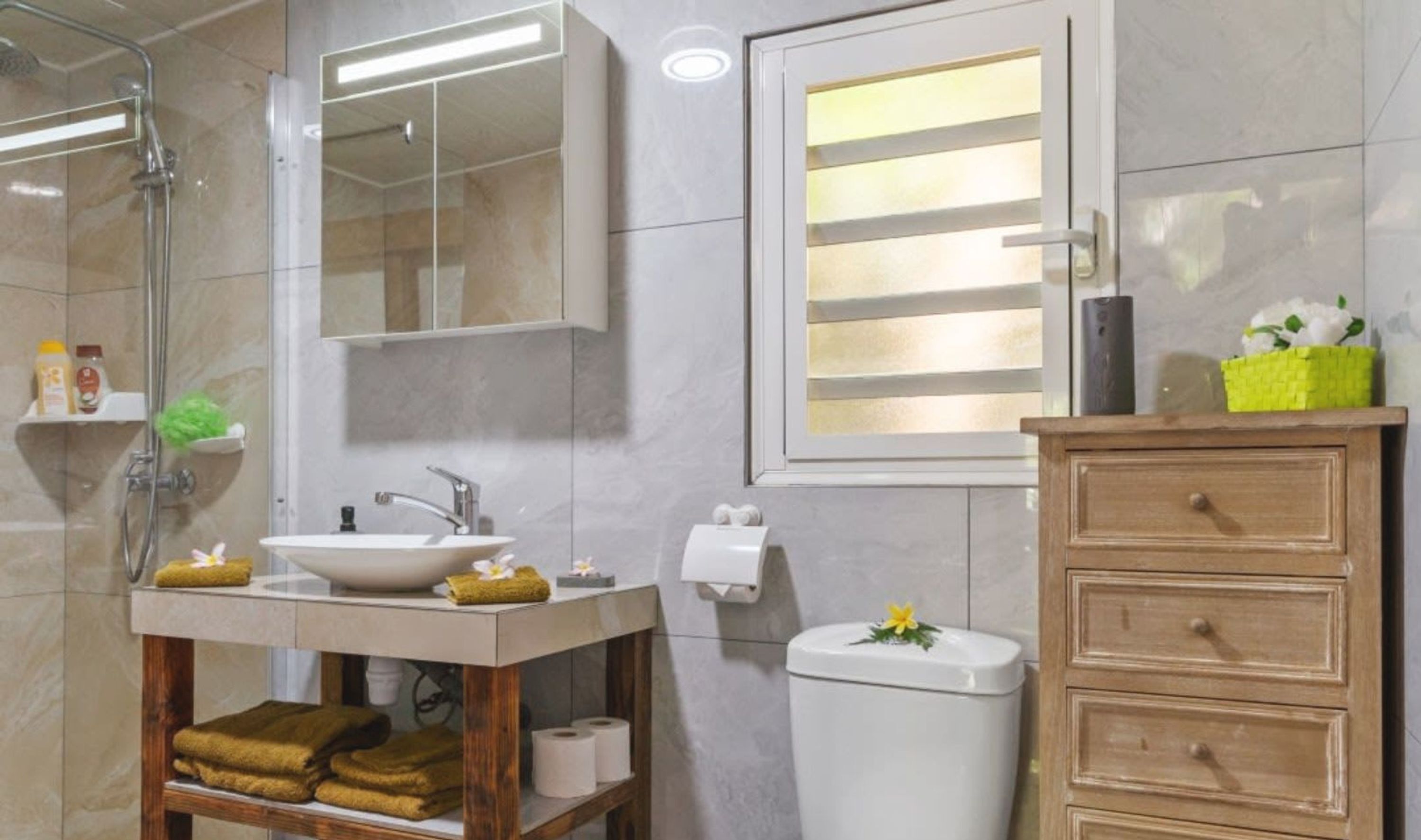 Een badkamer met een douchecabine van glas, een wastafel met spiegel, een toilet en een houten opbergmeubel met lades.