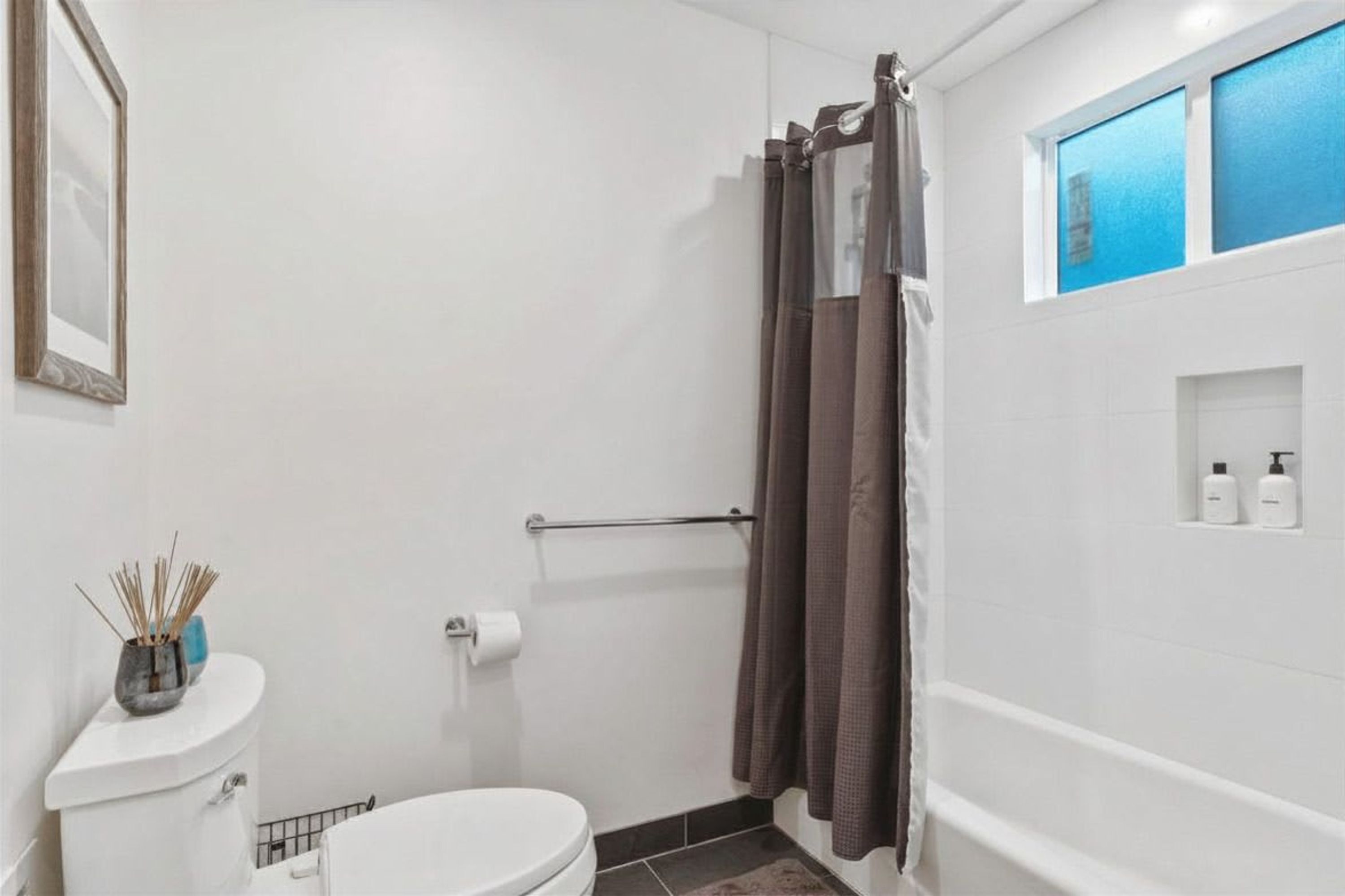 Et badeværelse med toilet, bruseforhæng og en hylde med toiletartikler.