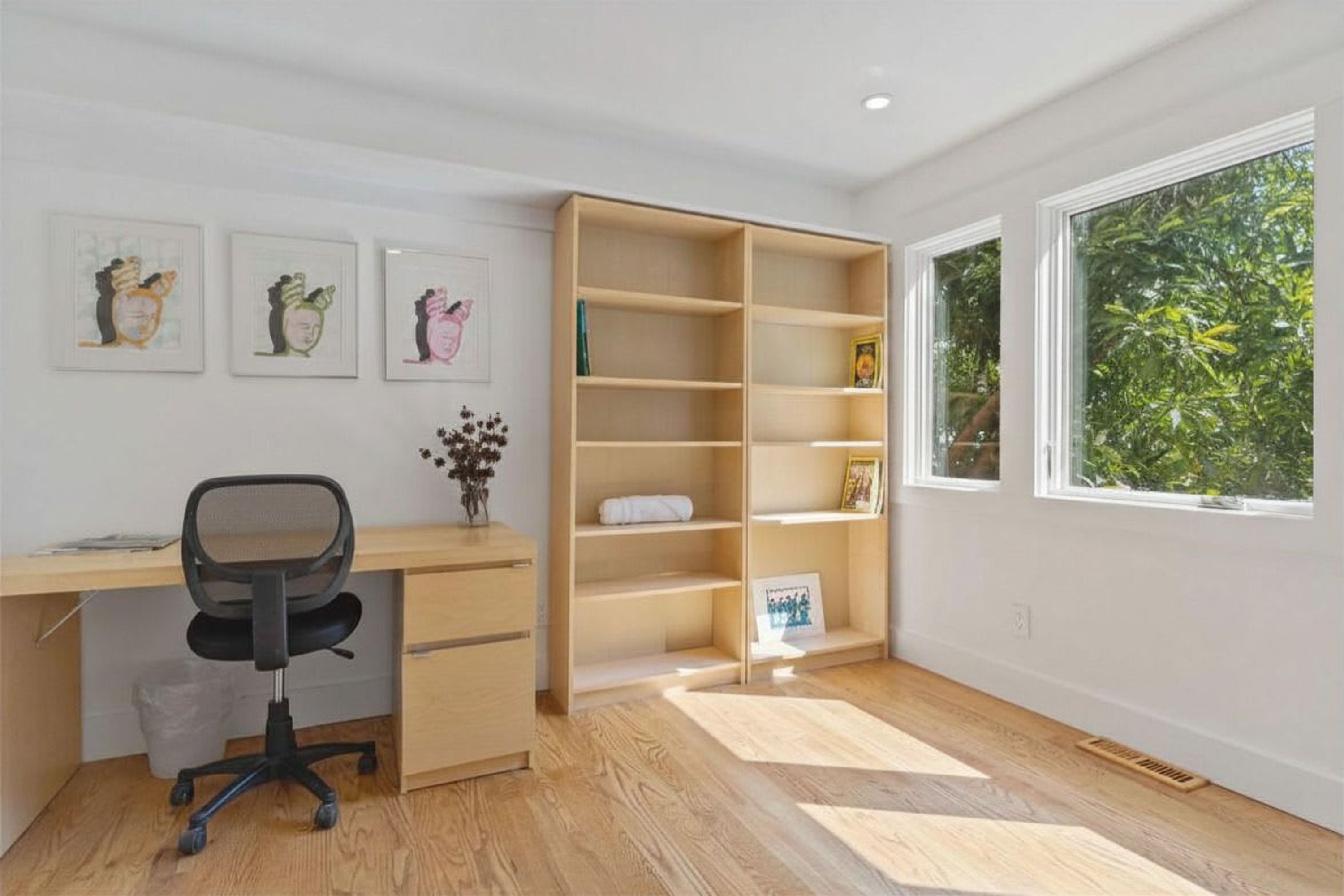 Una stanza con una scrivania in legno, una sedia da ufficio nera, una libreria e una finestra vista sul verde.