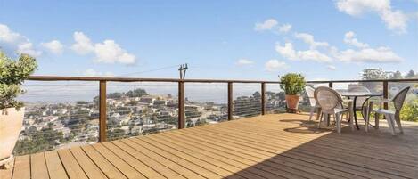 A wooden deck with a table and chairs, overlooking a cityscape.