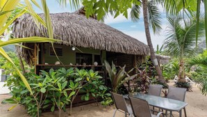 A thatched-roof hut with a table and chairs, surrounded by tropical plants and palm trees. - Beachfront Bungalows With Sunset Views in Haapiti (Moorea-Maiao)