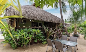 A thatched-roof hut with a table and chairs, surrounded by tropical plants and palm trees. - Beachfront Bungalows With Sunset Views in Haapiti (Moorea-Maiao)