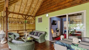 A room with a wooden ceiling, green walls, wicker furniture, a television, and a view of the outside. - Beachfront Bungalows With Sunset Views in Haapiti (Moorea-Maiao)