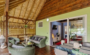 A room with a wooden ceiling, green walls, wicker furniture, a television, and a view of the outside. - Beachfront Bungalows With Sunset Views in Haapiti (Moorea-Maiao)