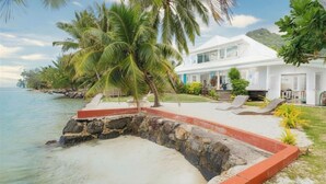 Una propiedad frente a la playa con una casa blanca, palmeras y una vista despejada del océano.