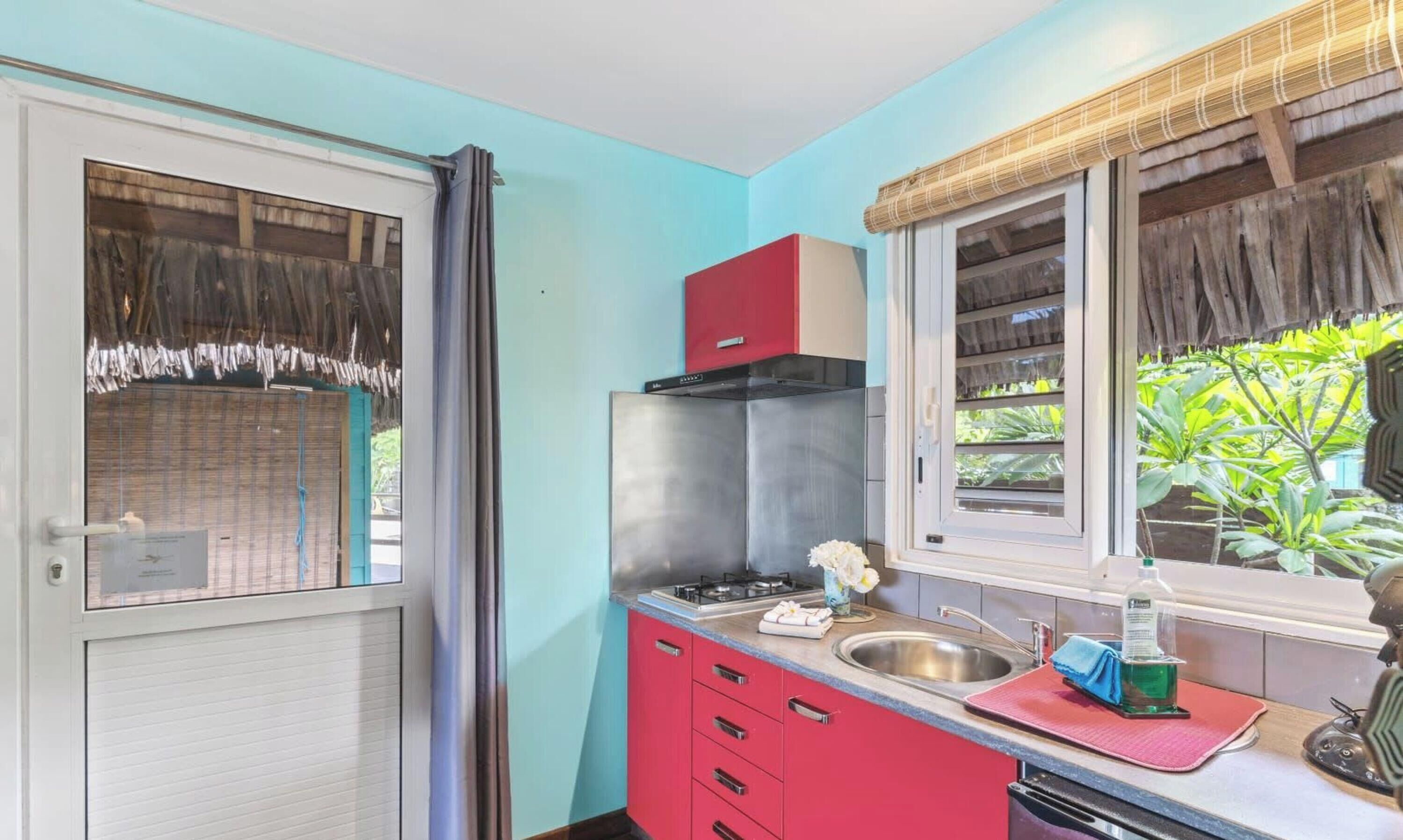 A compact kitchen with a gas stove, a sink, and a red cabinet.