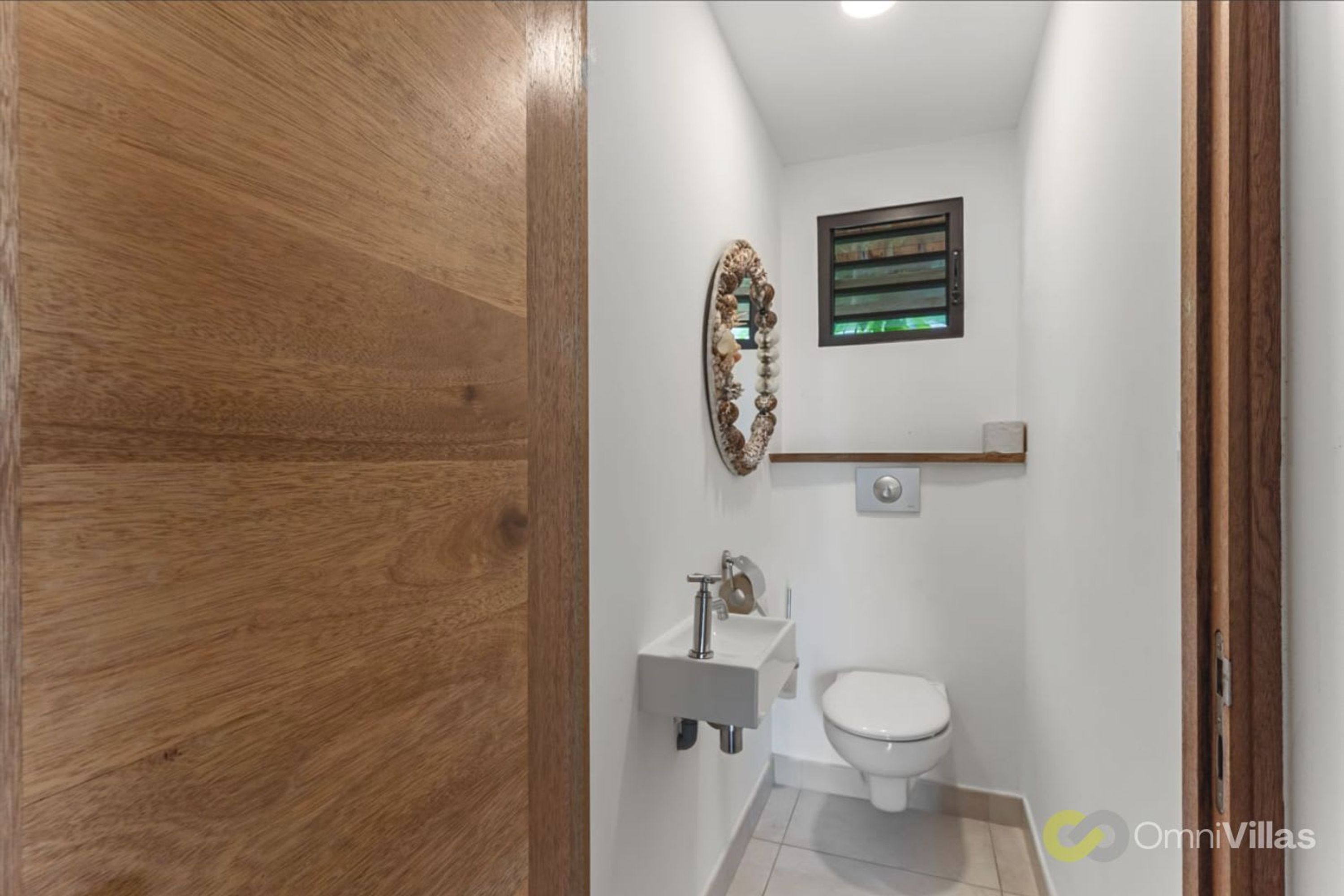 Une salle de bain avec une porte en bois, un lavabo blanc, des toilettes et un miroir décoratif.