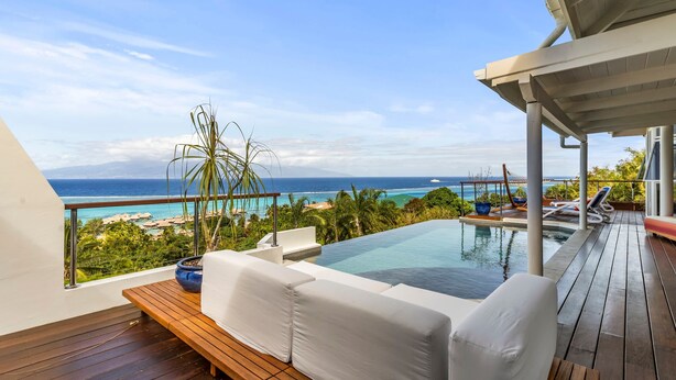 Ein Balkon mit Holzboden, weißen Möbeln für draußen, einem kleinen Pool und Blick auf den Ozean.