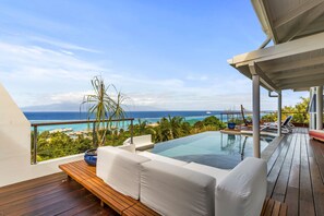 Un balcón con piso de madera, mobiliario exterior blanco, una pequeña piscina y vista al océano.