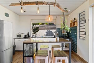 A kitchen with a wooden ceiling, hanging light bulbs, a central island with stools, a microwave, and a sink.