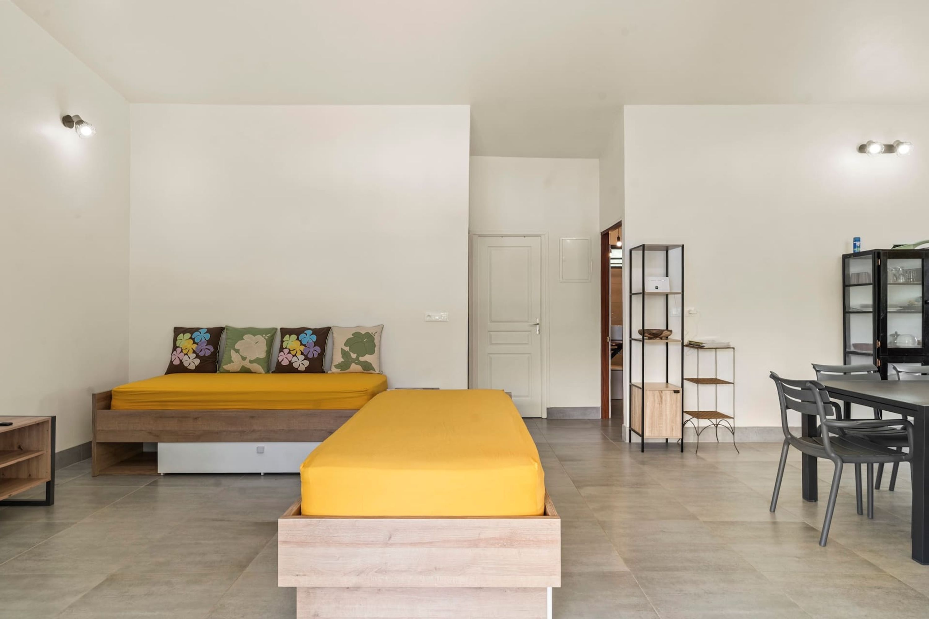 A modern room with a bed, a bench, a dining area, and a small kitchen.