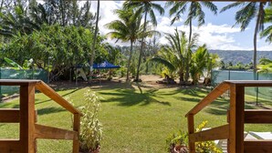 A view from a wooden deck with a grassy yard, palm trees, and a tennis court in the background. - Temenino Pihiti Secluded Bungalow (Taiarapu-Ouest)