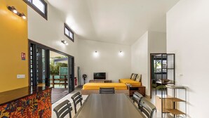 A modern room with a dining table, chairs, a sofa, a TV, and a small table with a shelf. - Temenino Pihiti Secluded Bungalow (Taiarapu-Ouest)